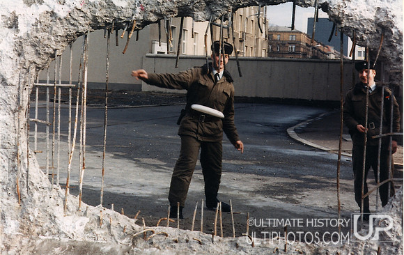 A guard throws a disc through the partially demolished Berlin Wall, 1990